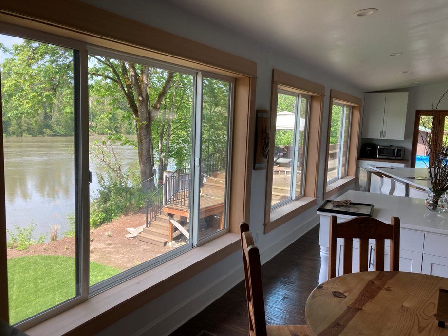 Sunlit dining room with floor-to-ceiling windows overlooking a river and trees