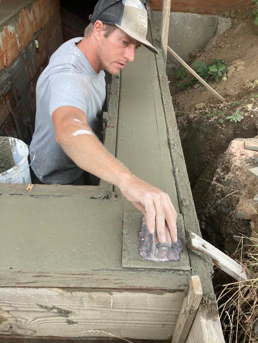 Worker smoothing wet concrete on a narrow foundation wall outdoors