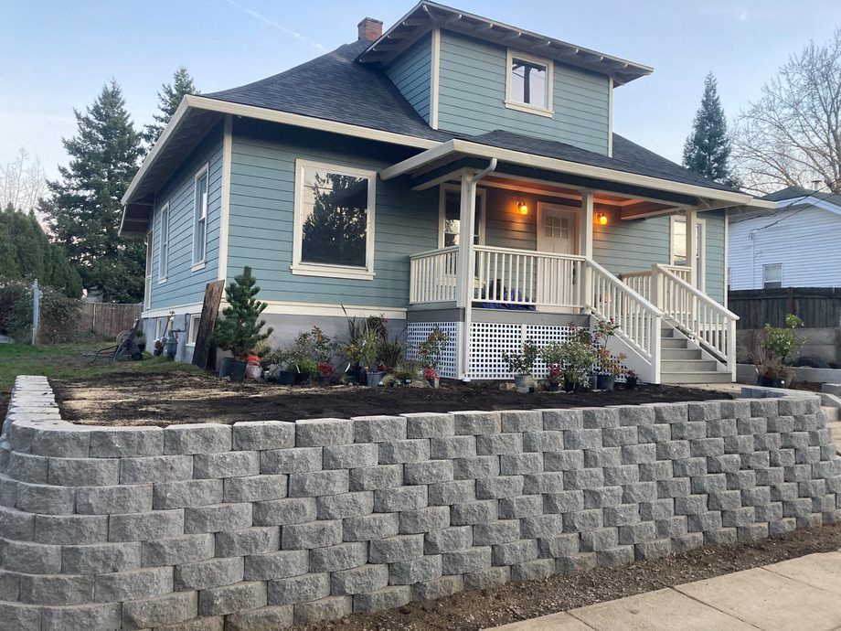 Blue house with lit porch and steep stone retaining wall in front yard