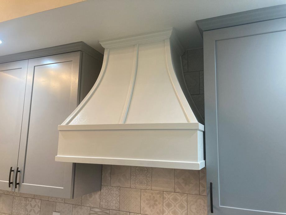 White kitchen range hood between gray cabinets over a tiled backsplash