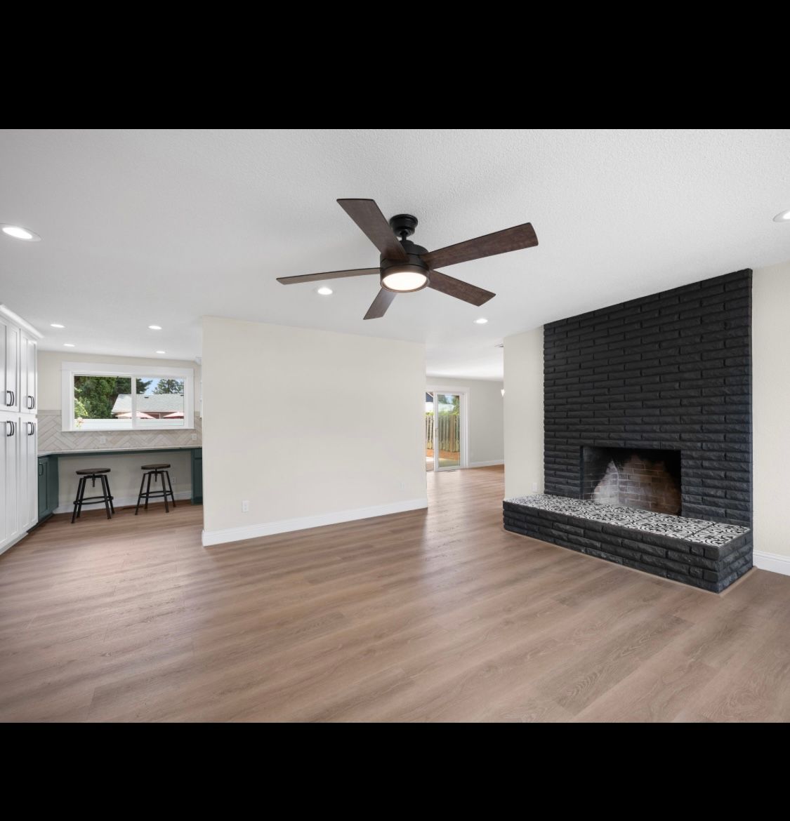 Spacious white living room with wood floors, ceiling fan, and black brick fireplace.