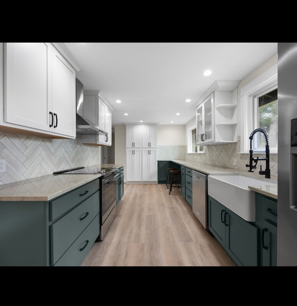 Bright modern kitchen with white and dark teal cabinets, wood floors, and a farmhouse sink.