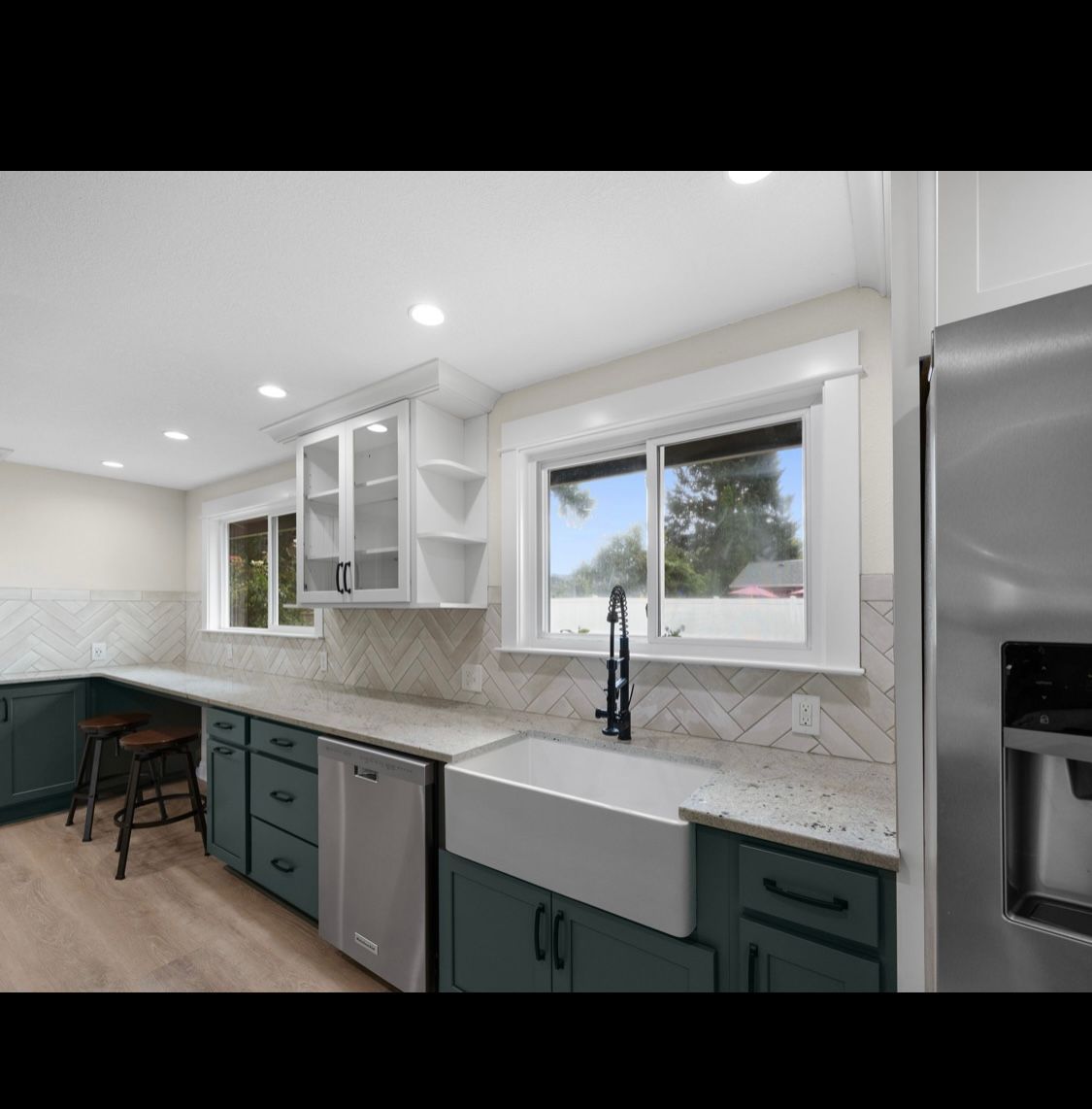 Modern white kitchen with green cabinets, farmhouse sink, stainless fridge, and bright window views