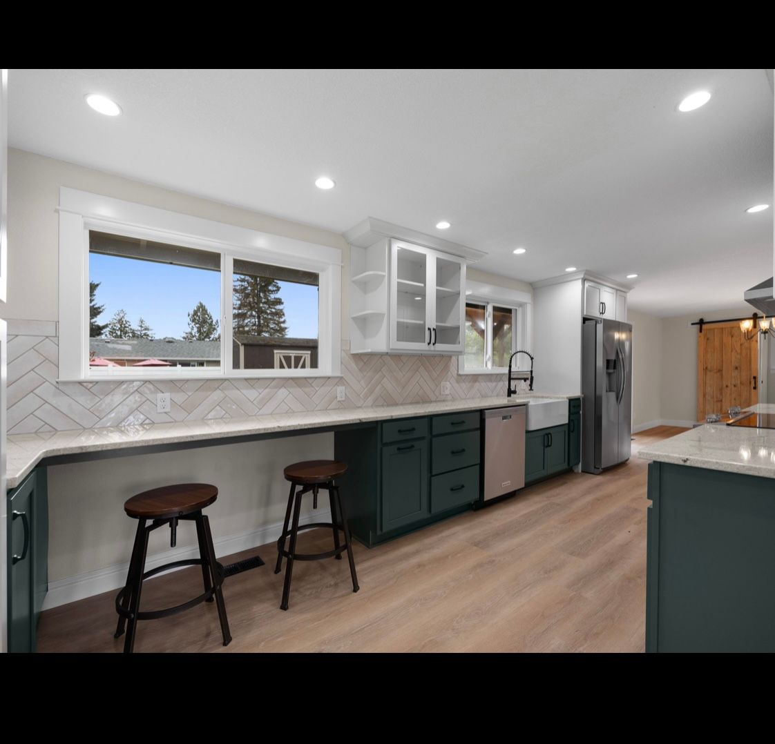 Bright modern kitchen with white cabinets, dark green lower cabinets, island stools, and stainless steel fridge