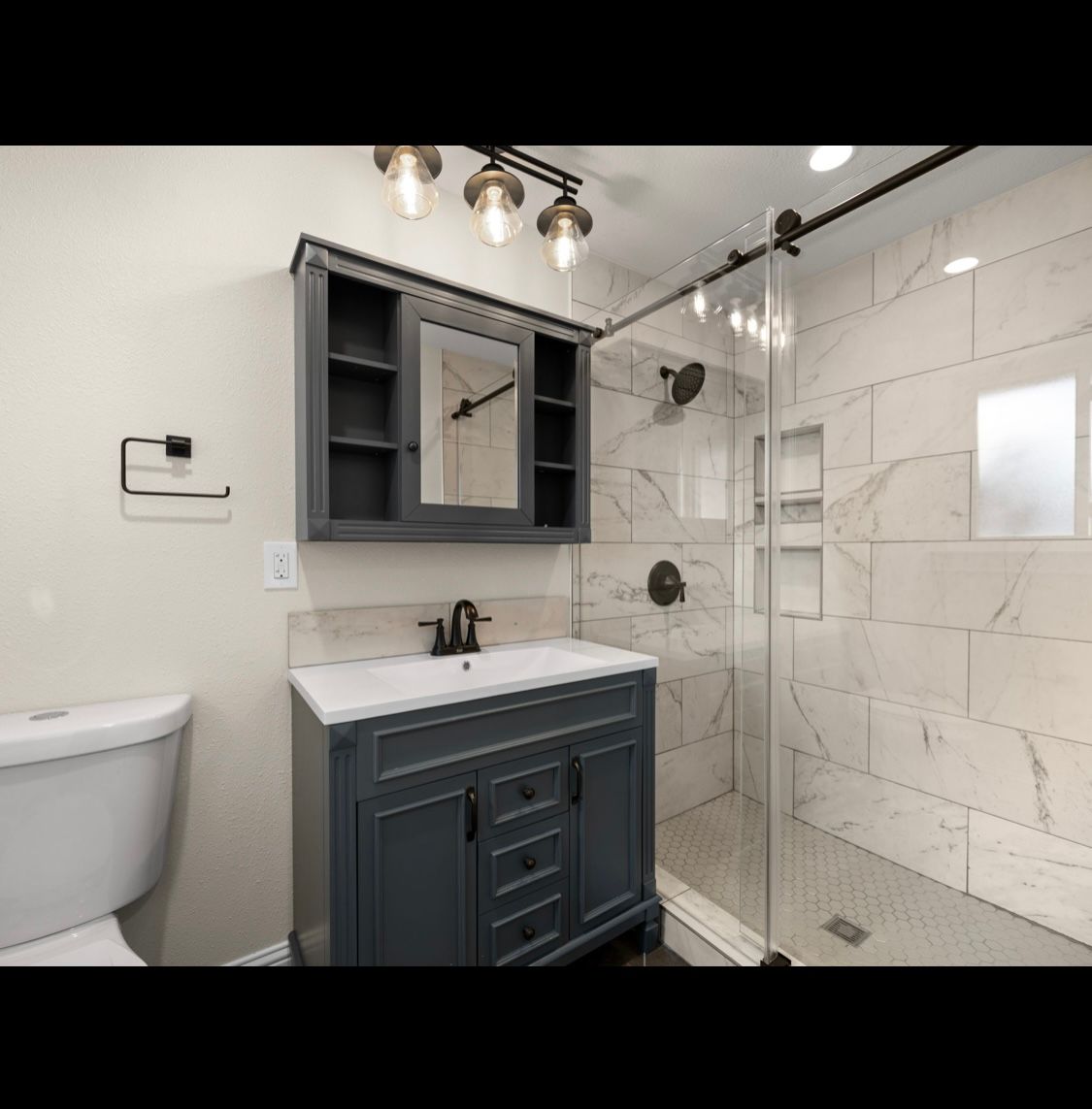 Modern bathroom with navy vanity, white marble shower, and glass shower door