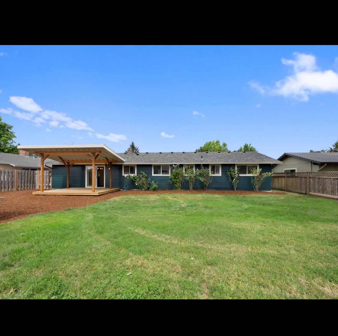 Single-story house with large green lawn, covered patio, and blue sky in the background
