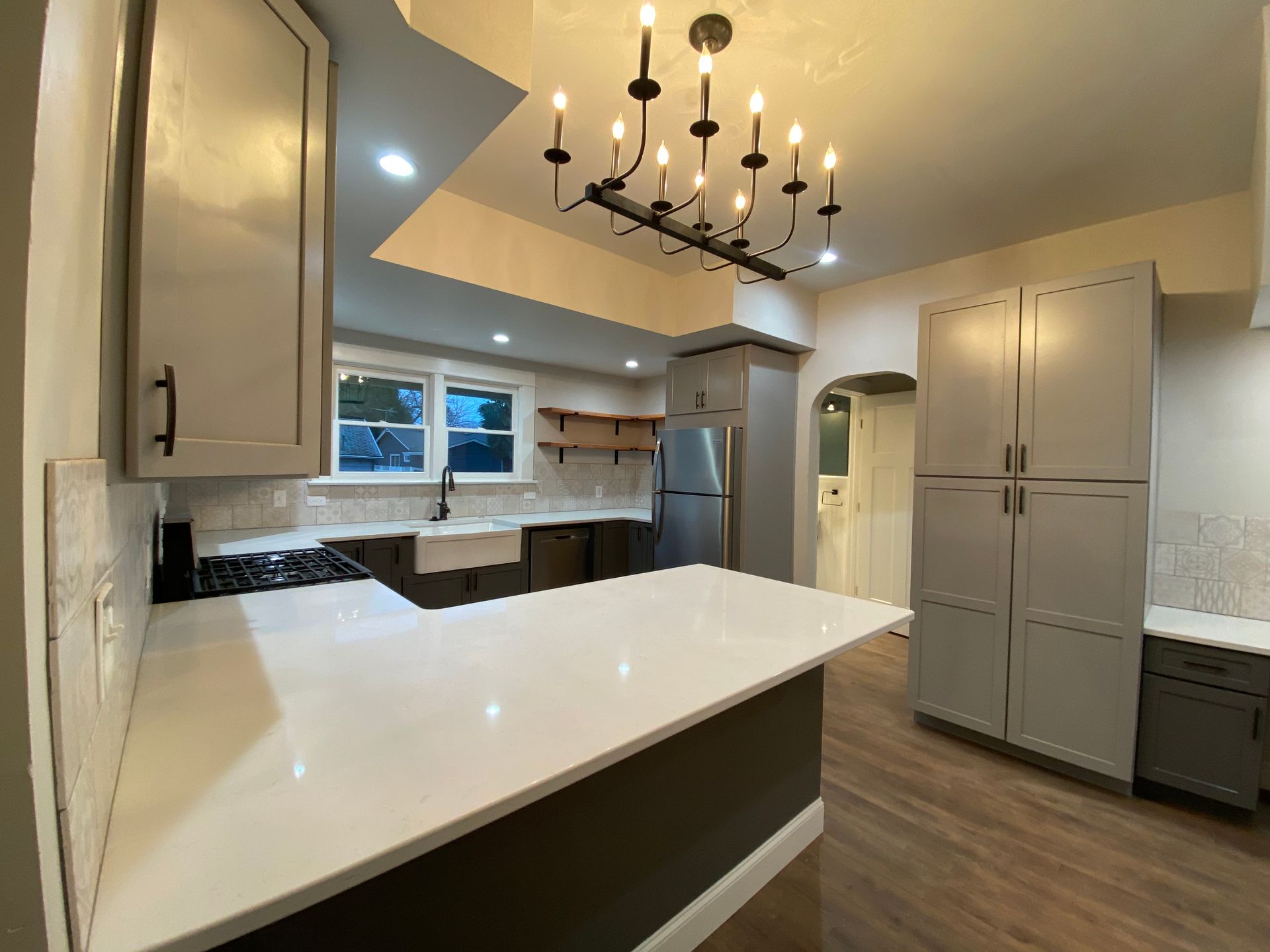 Modern kitchen with white countertops, gray cabinets, wood floors, and a black chandelier above the island