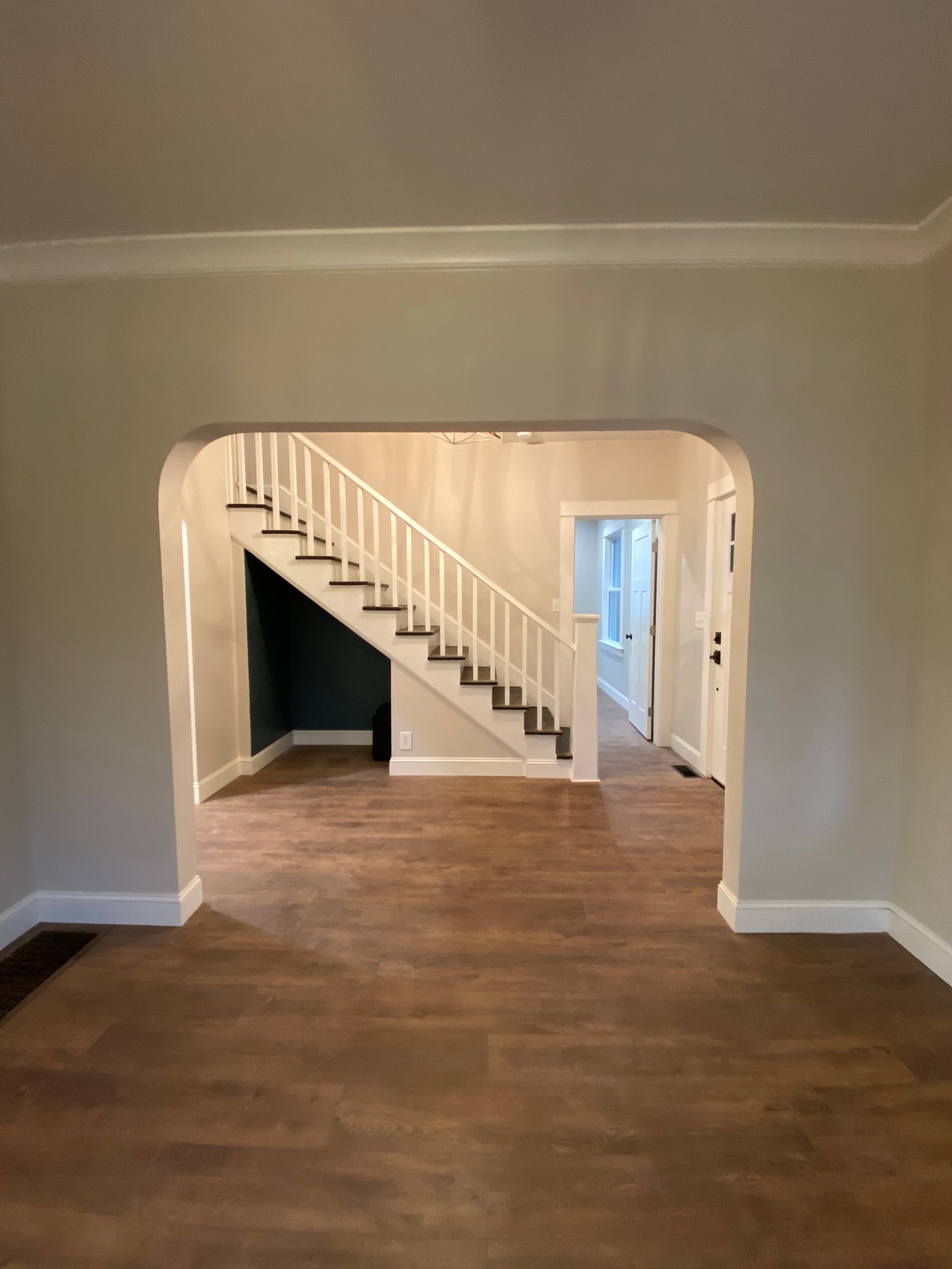Empty living room with hardwood floor, archway, and staircase leading to a hallway