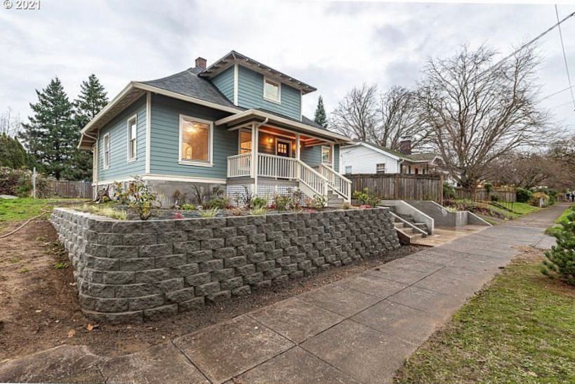 Blue house with front porch, stone retaining wall, and sloped driveway in a suburban yard.