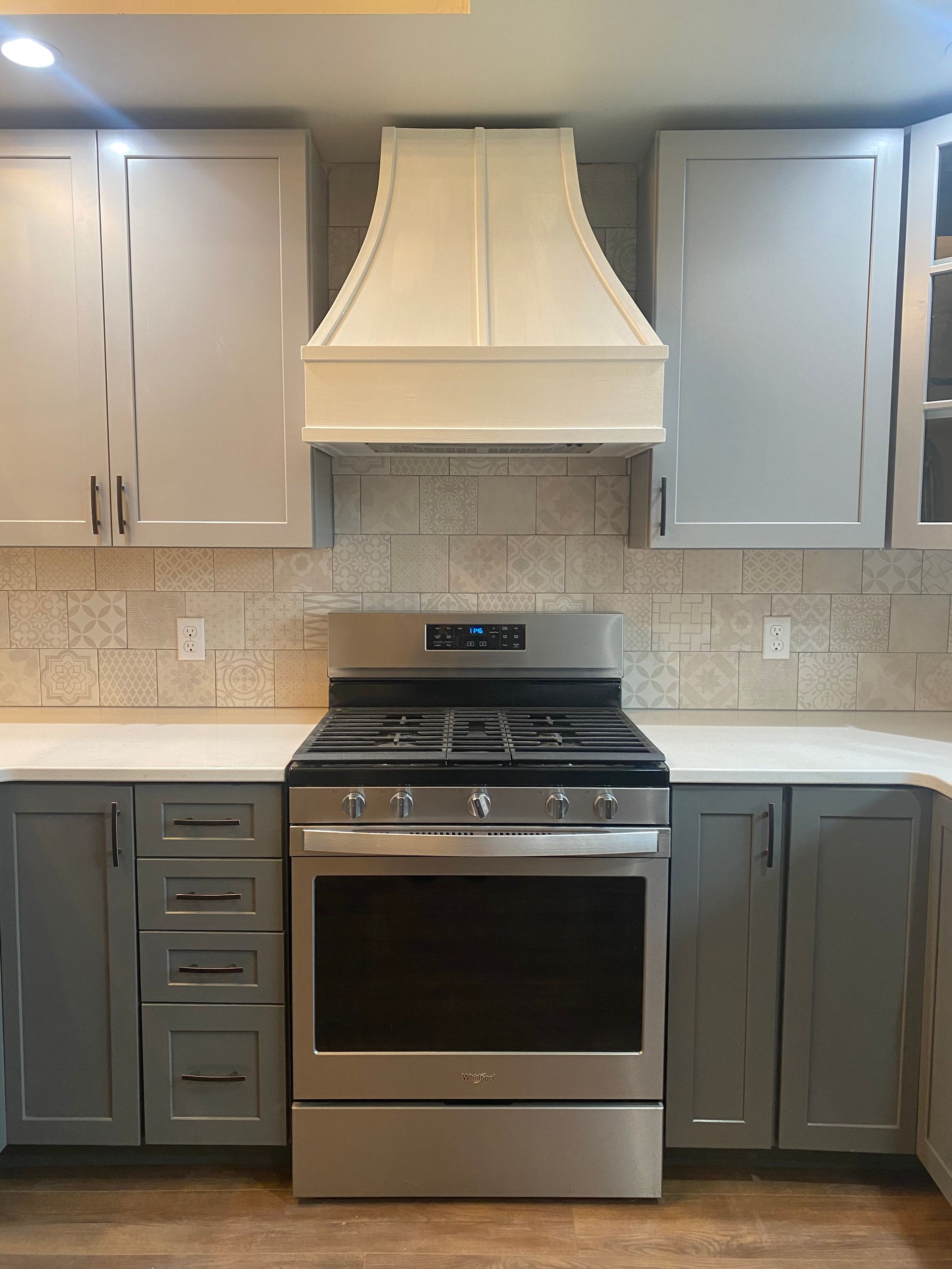 Modern kitchen with white and gray cabinets, stainless steel stove, and white range hood