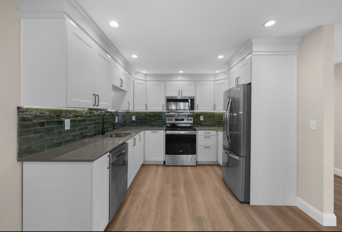 Modern white kitchen with green tile backsplash, stainless appliances, and light wood floors
