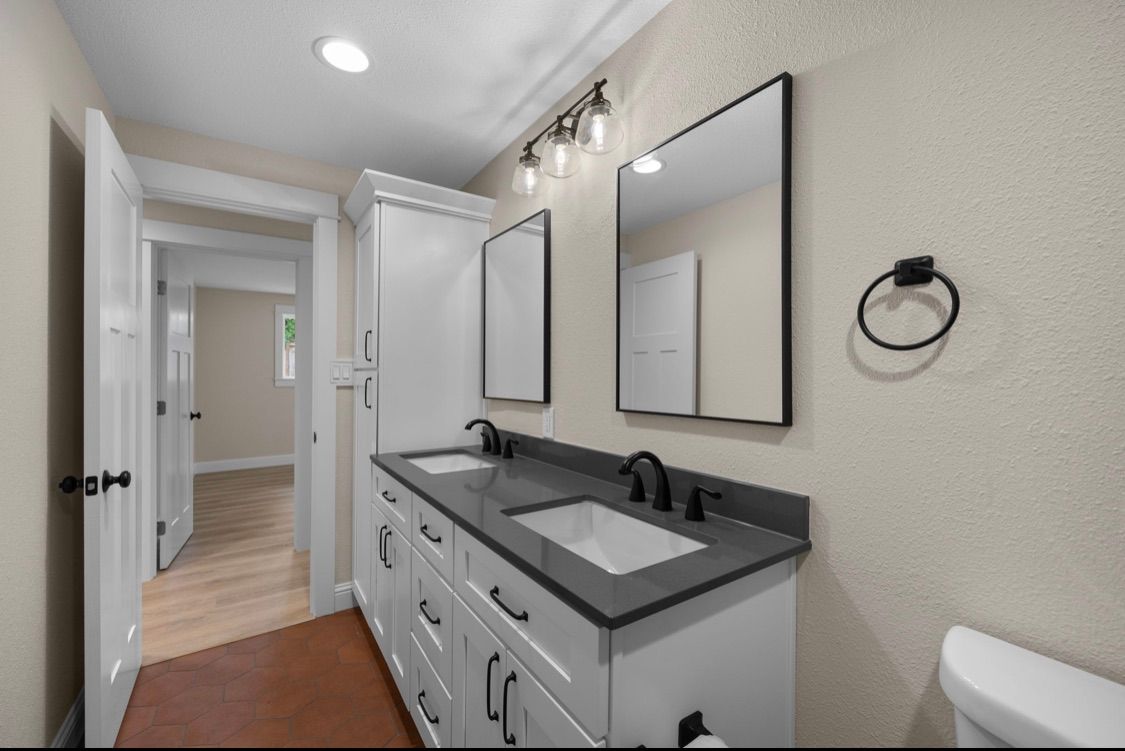 Modern bathroom vanity with double mirrors, gray countertop, black fixtures, and a hallway view beyond