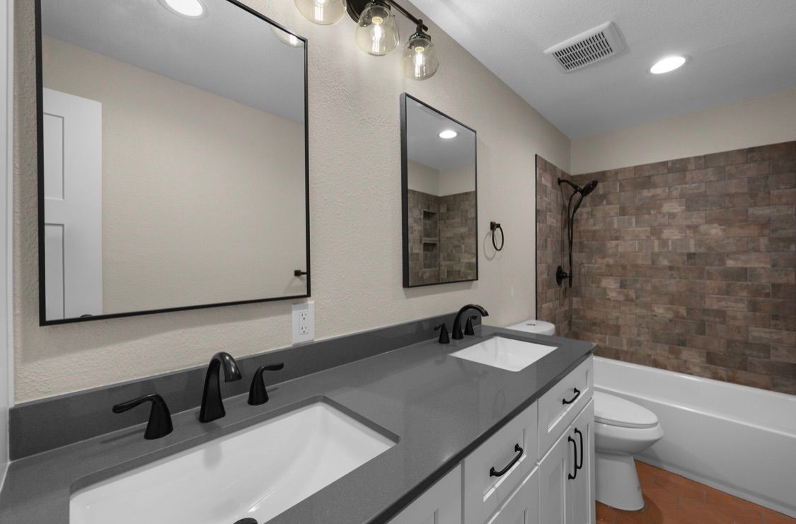 Modern bathroom with double vanity, large mirrors, and a tiled tub/shower area