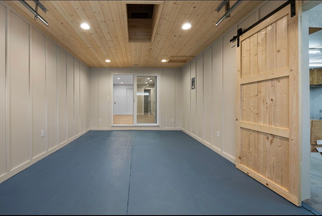 Empty room with blue carpet, white paneled walls, wood ceiling, and a large wooden sliding door.