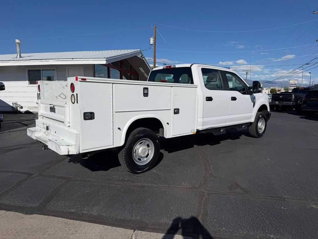 White utility truck with service body parked on asphalt under a clear blue sky