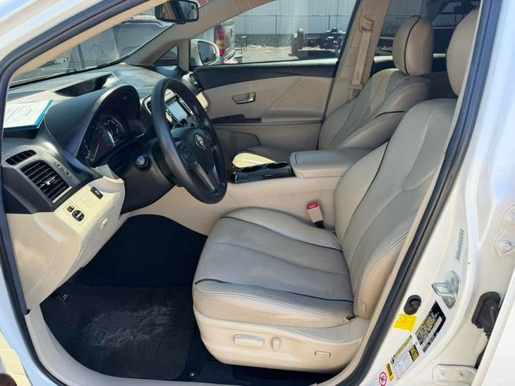 Car interior with beige leather seats and steering wheel, viewed through the open driver’s door