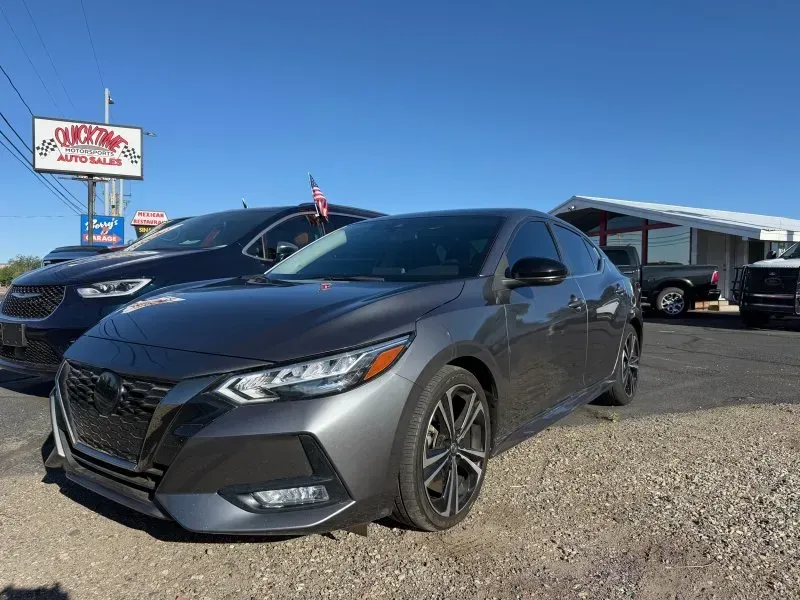 Dark gray sedan parked at a car dealership lot on a sunny day.