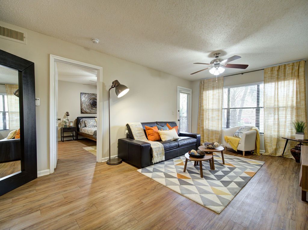 Bright living room with a gray sofa, coffee tables, patterned rug, and sunlight through large windows at Grande Oasis at Carrollwood in Tampa, Florida.