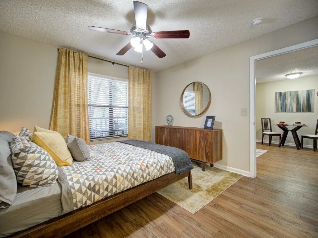 Bedroom with a bed, ceiling fan, dresser, and open doorway to a dining area at Grande Oasis at Carrollwood in Tampa, Florida.