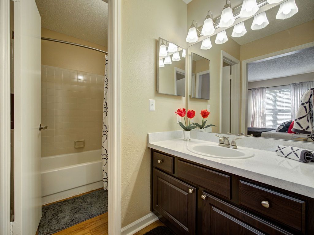 Bathroom vanity with dark wood cabinets, large mirror, flowers, and a tub visible through the open door at Grande Oasis at Carrollwood in Tampa, Florida.