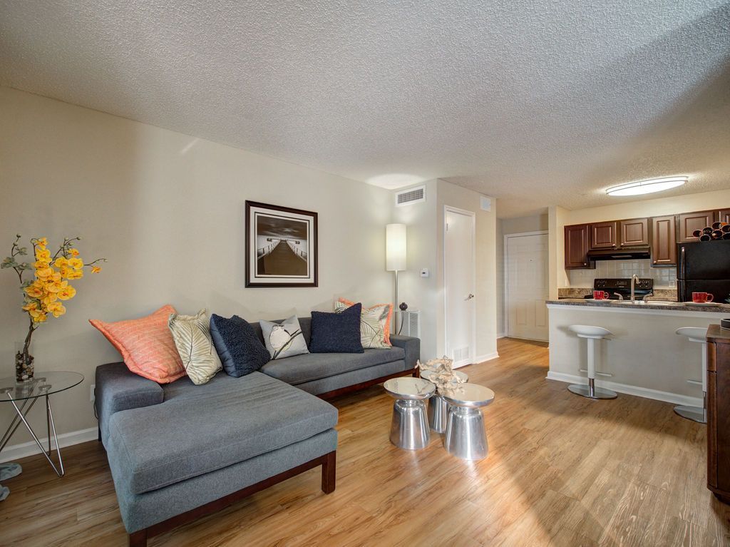 Bright living room with gray sofa, pillows, coffee table, and open kitchen with wood cabinets at Grande Oasis at Carrollwood in Tampa, Florida.