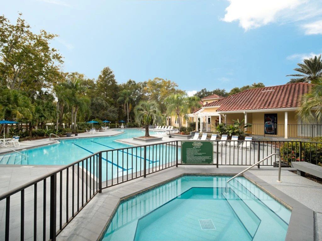 Resort pool area with a hot tub, turquoise pool, palm trees, and a tiled building with a red roof at Grande Oasis at Carrollwood in Tampa, Florida.