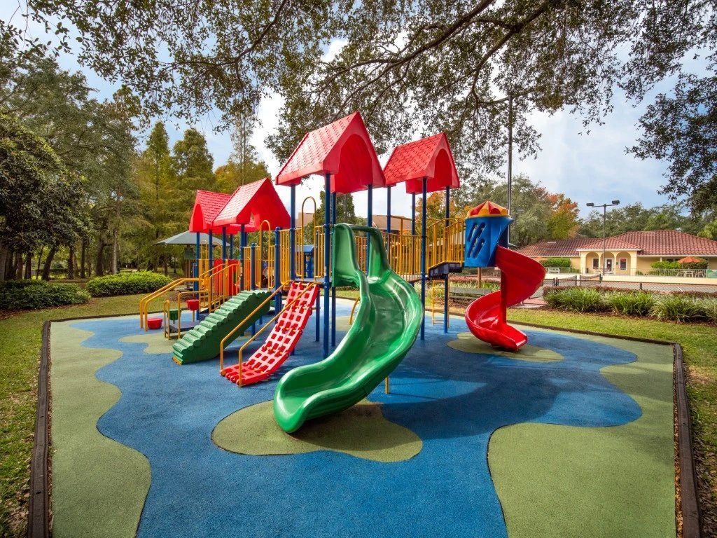 Colorful playground with slides and climbing structures on a rubber play surface under trees at Grande Oasis at Carrollwood in Tampa, Florida.