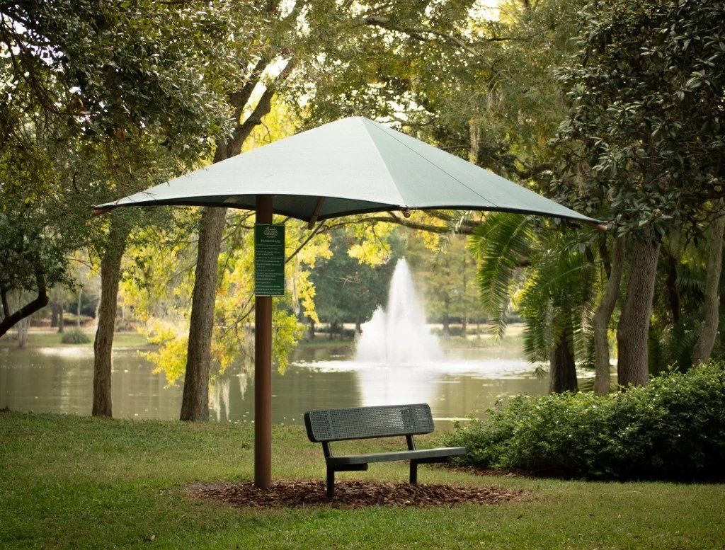 Park bench under a white canopy near a pond fountain in a tree-lined park at Grande Oasis at Carrollwood in Tampa, Florida.