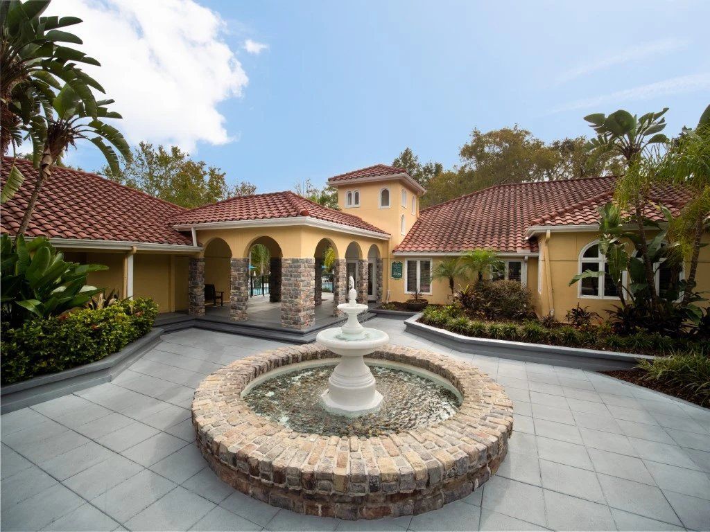 Courtyard with central fountain, tiled walkways, and Mediterranean-style buildings with red roofs around it at Grande Oasis at Carrollwood in Tampa, Florida.