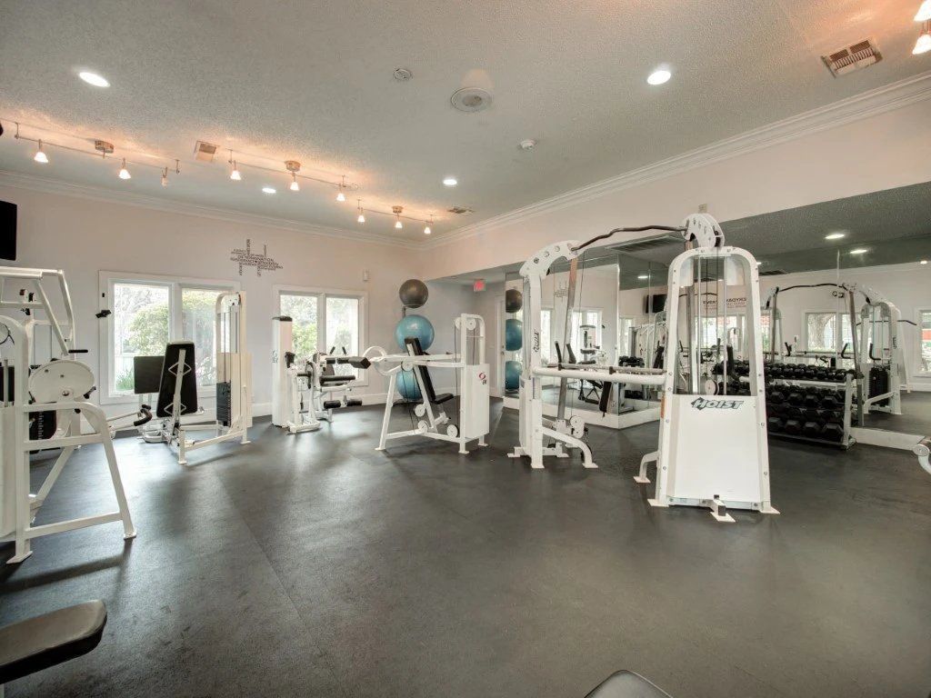 Bright gym interior with cardio and weight machines, mirrored walls, and a person exercising in the center at Grande Oasis at Carrollwood in Tampa, Florida.