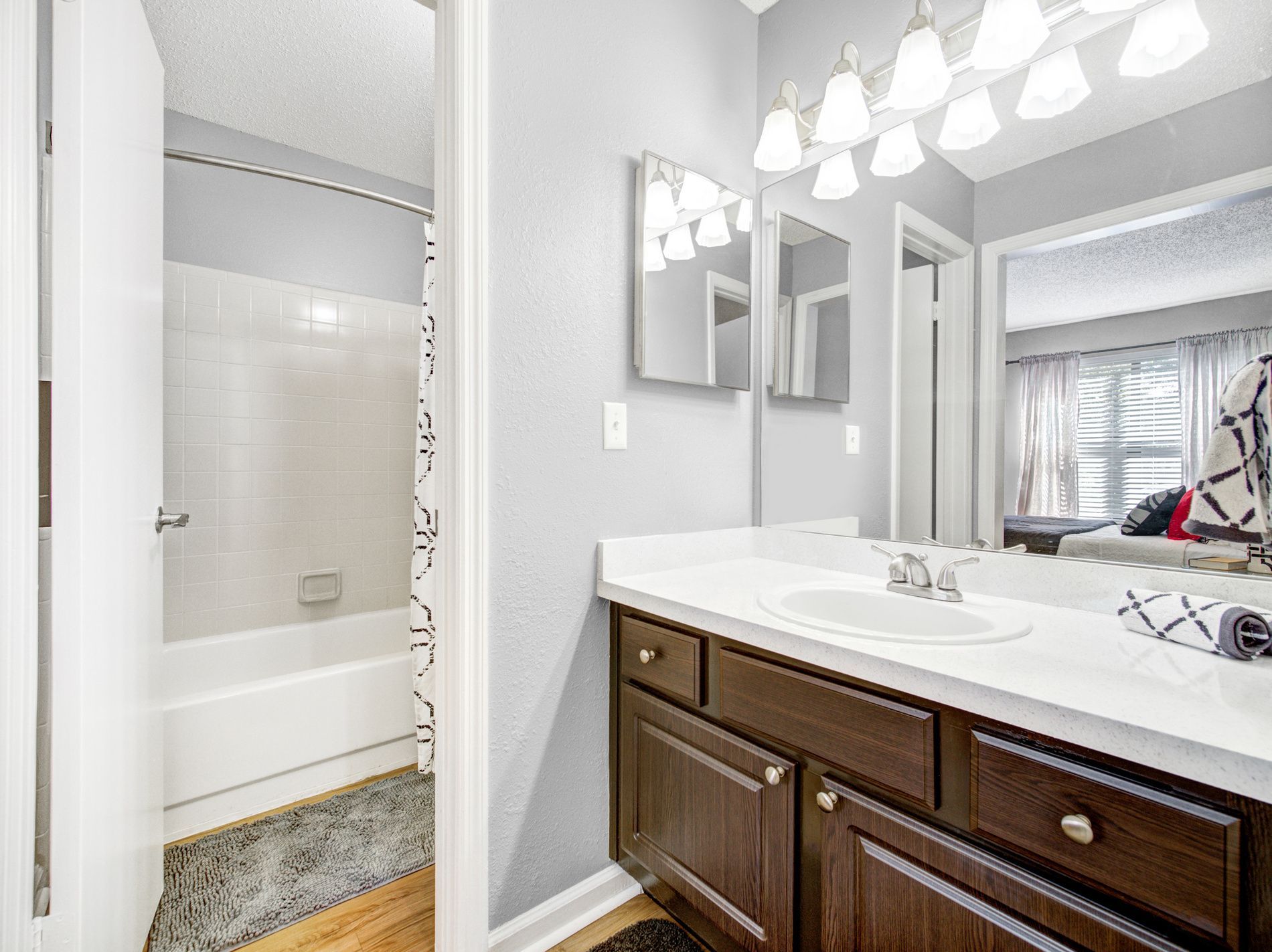 Bathroom vanity with mirror lights beside a bathtub and shower curtain in a light gray room at Grande Oasis at Carrollwood in Tampa, Florida.