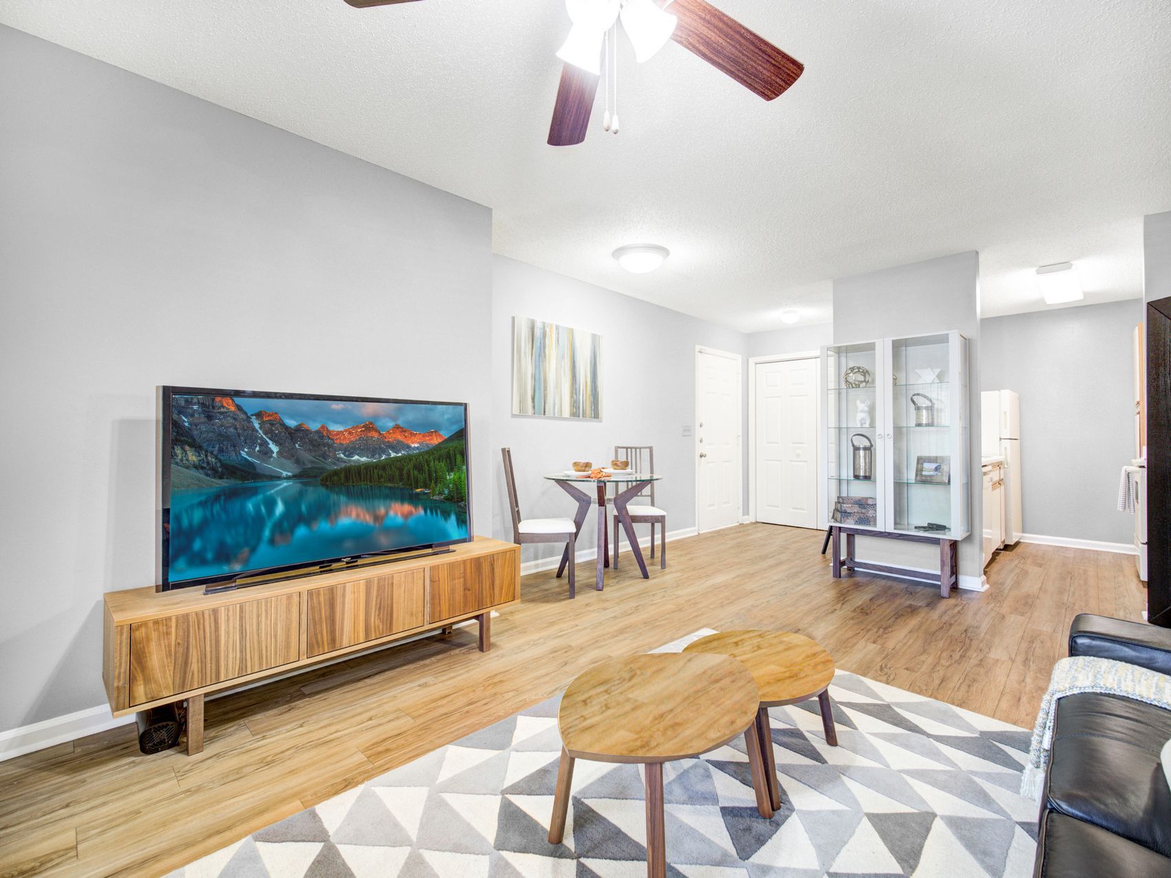 Modern living room with TV, coffee table, rug, wood floors, and ceiling fan; bright, open layout at Grande Oasis at Carrollwood in Tampa, Florida.