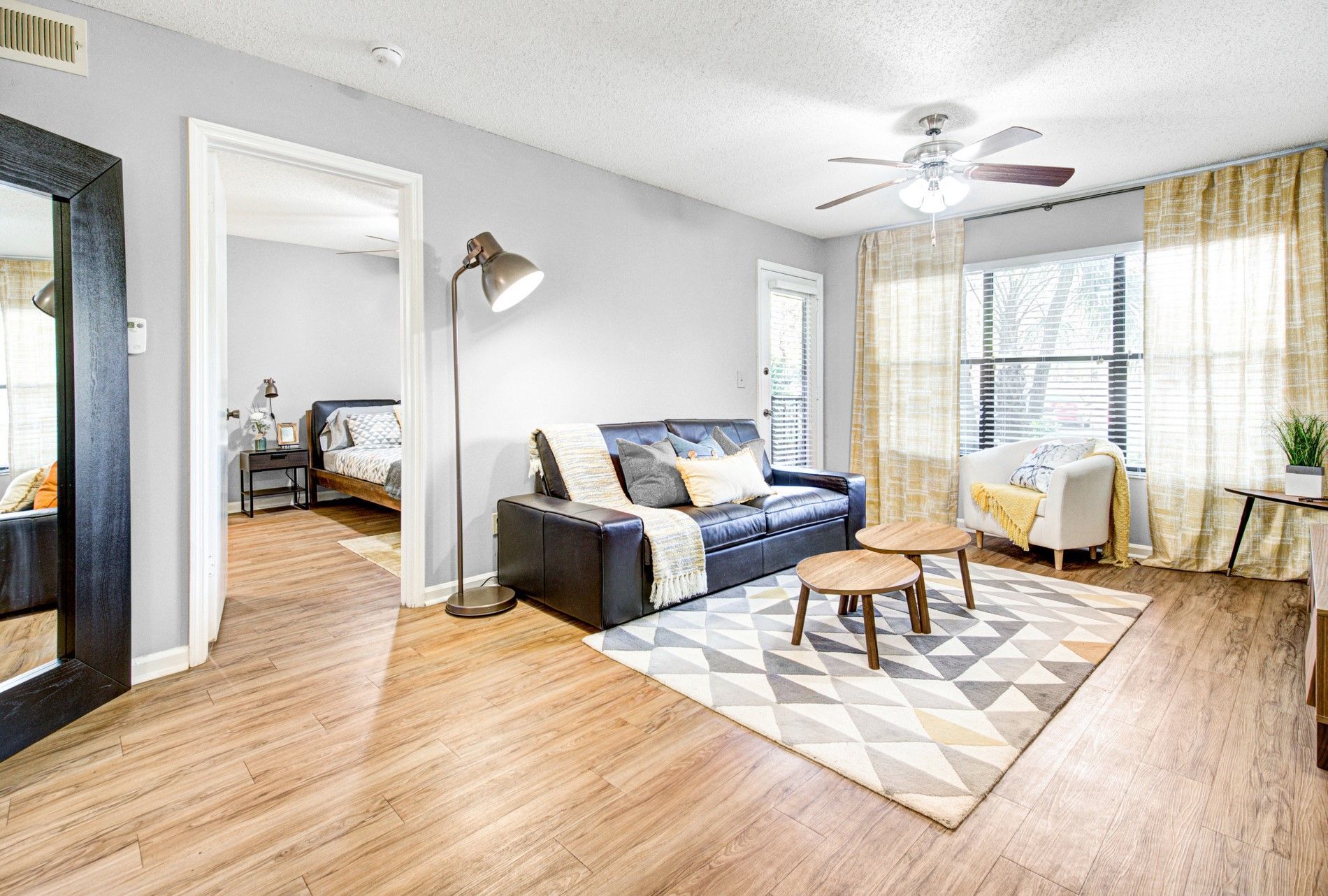Bright living room with blue sofa, round coffee table, patterned rug, and large windows with curtains at Grande Oasis at Carrollwood in Tampa, Florida.