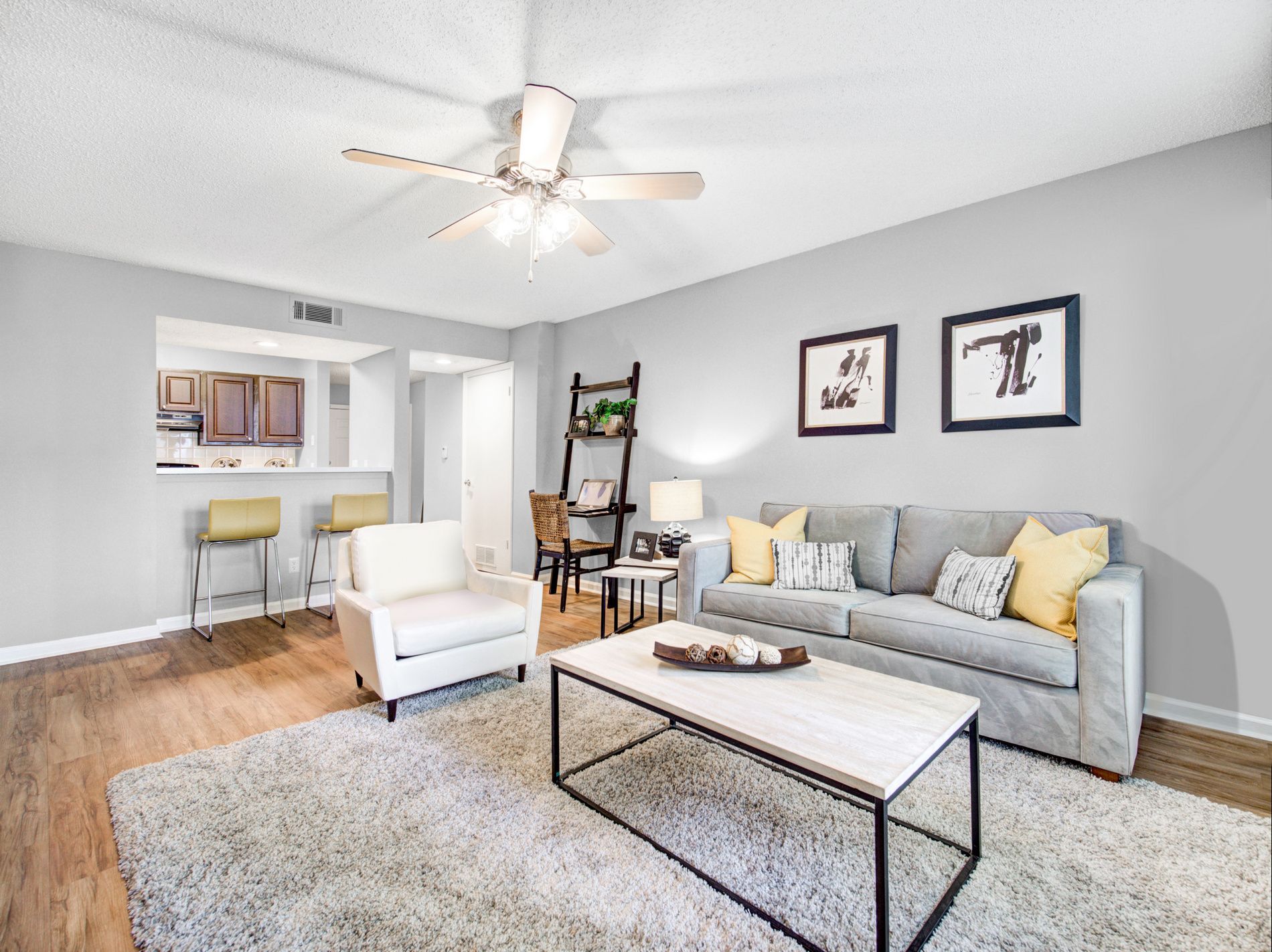 Bright living room with gray sofa, white chair, coffee table, rug, and ceiling fan near kitchen pass-through at Grande Oasis at Carrollwood in Tampa, Florida.