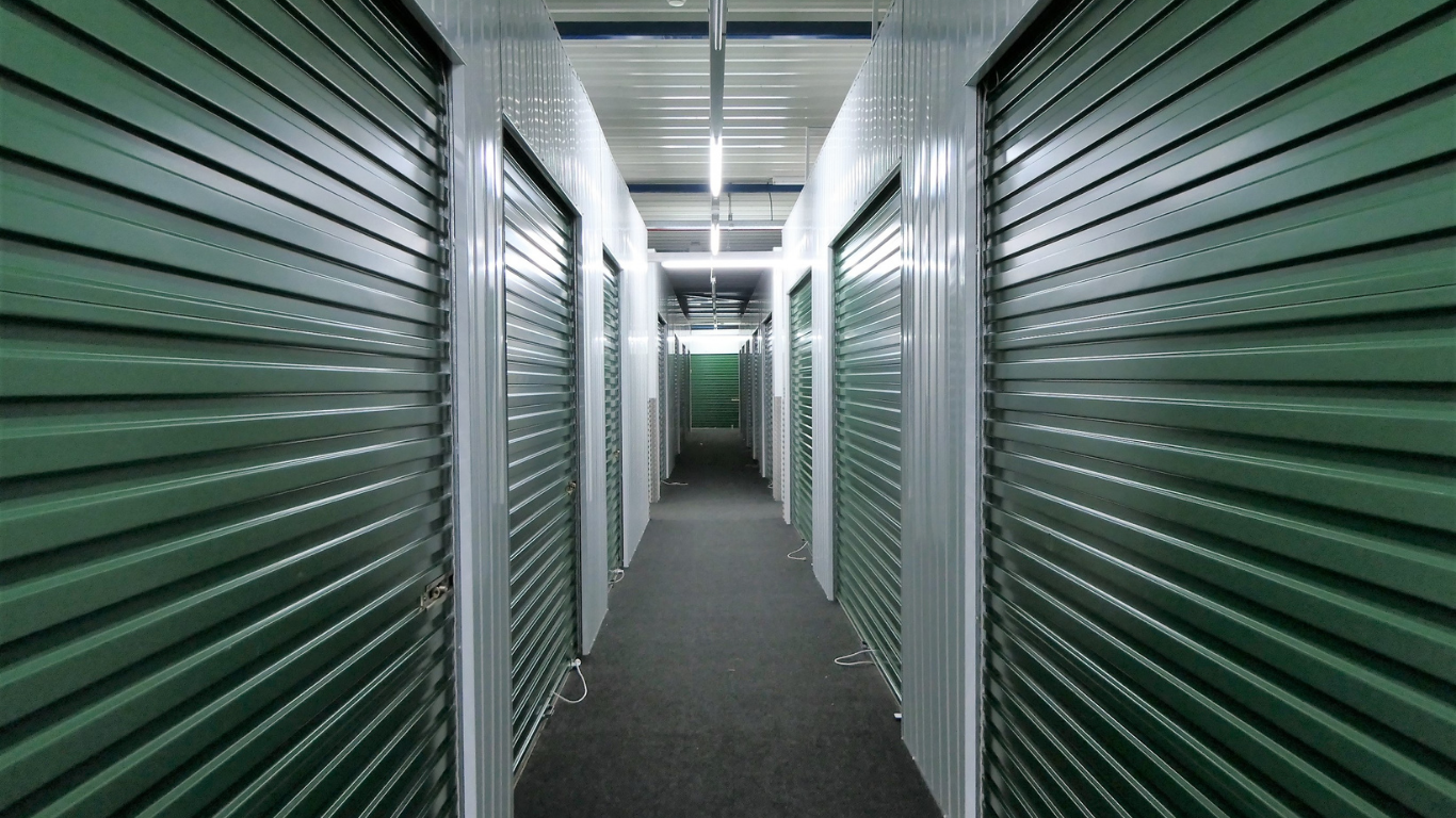 Row of blue and white storage unit doors along a gravel driveway