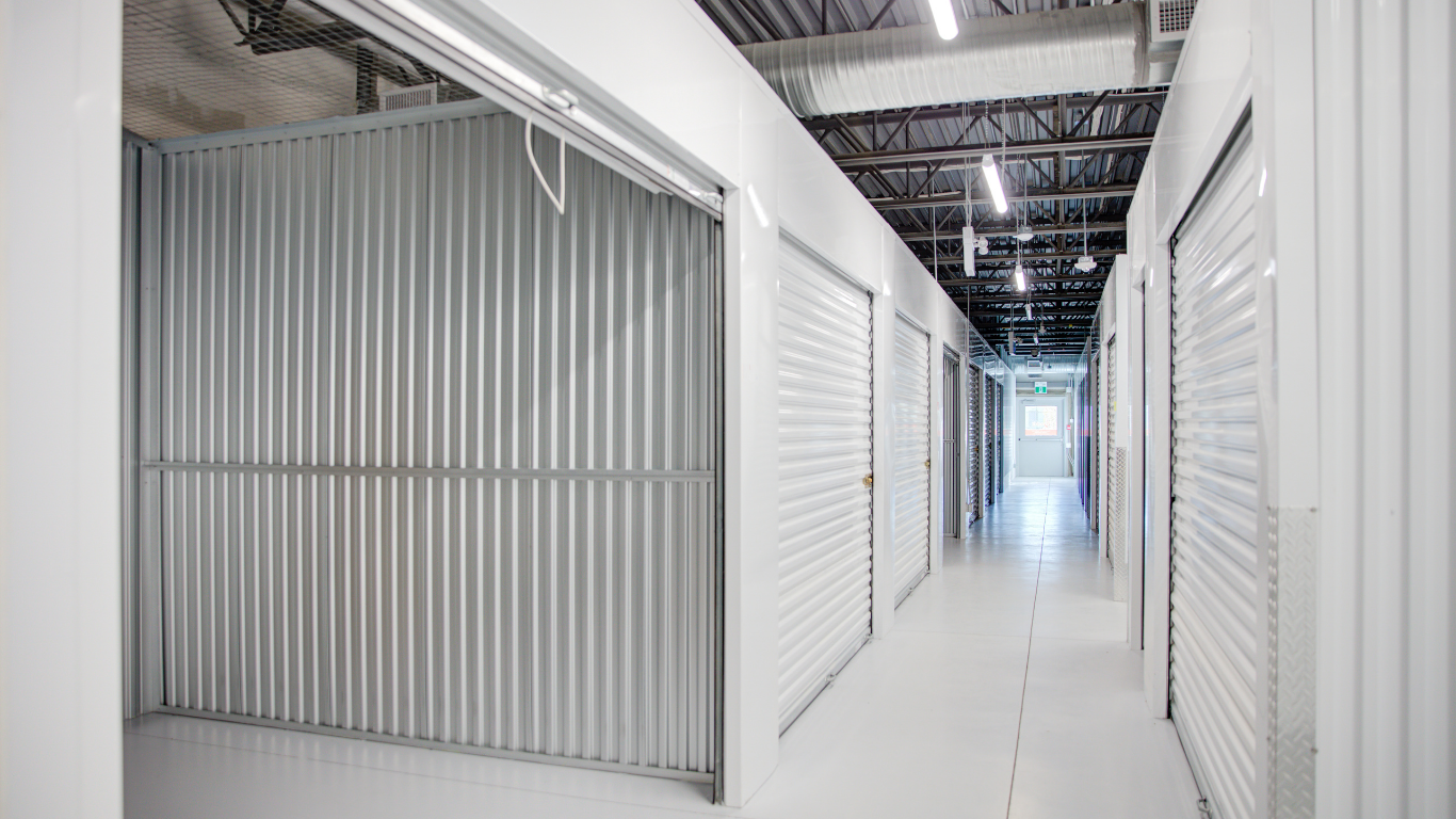 Row of white storage unit doors beside a gravel drive under a clear sky