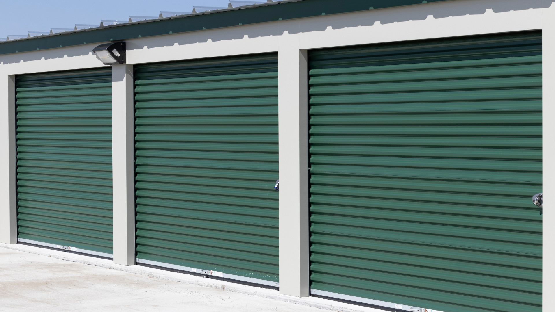 Three green roll-up storage doors on a white building exterior