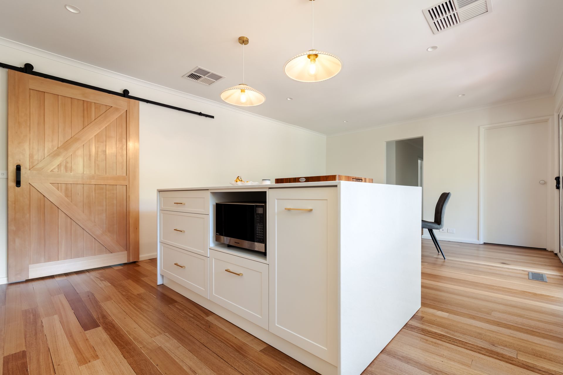 Bright modern kitchen with wood floors, island cabinets, and pendant lights, viewed from the open living area