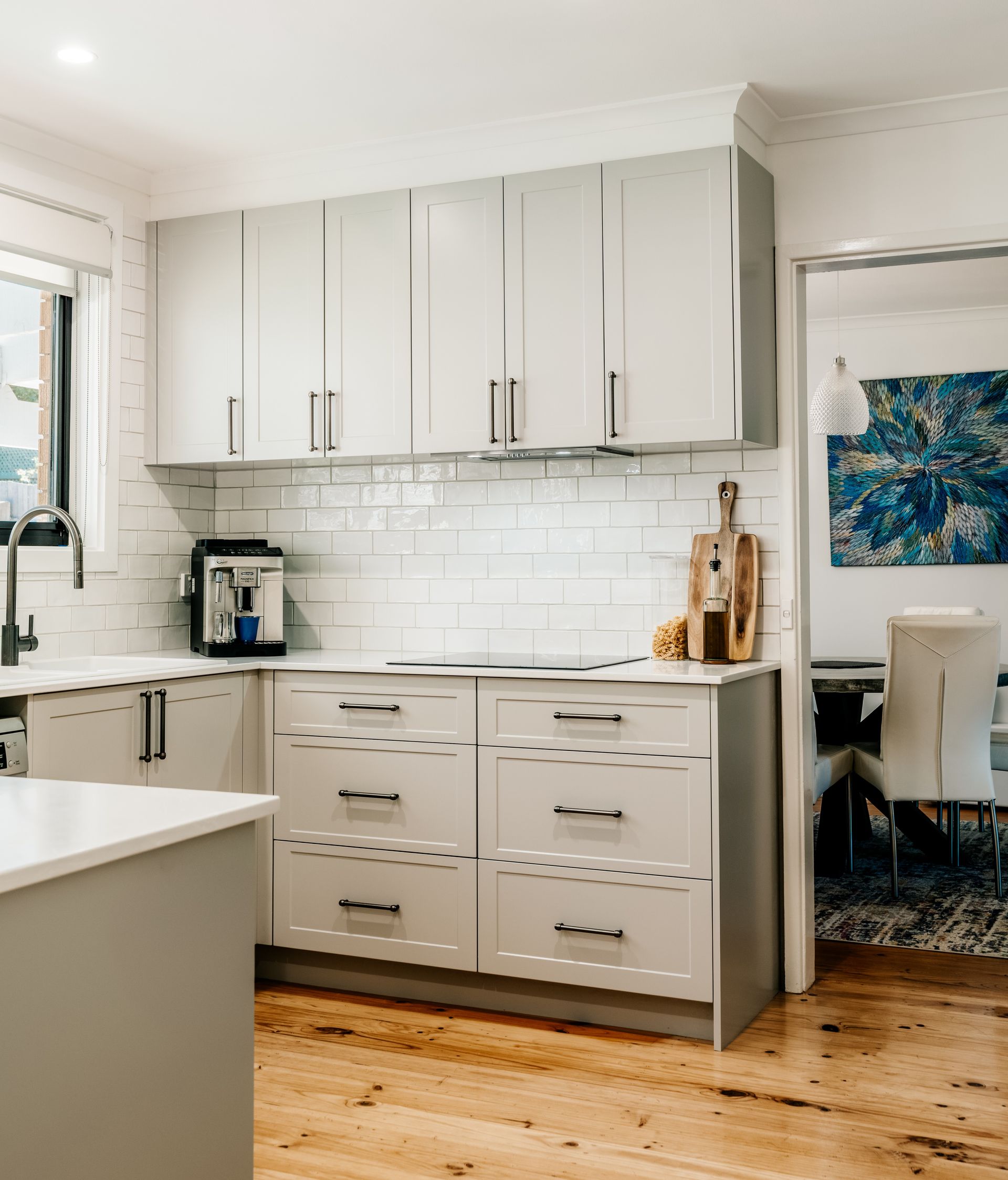Bright white kitchen with cabinets, subway tile backsplash, coffee maker, and wooden floor.