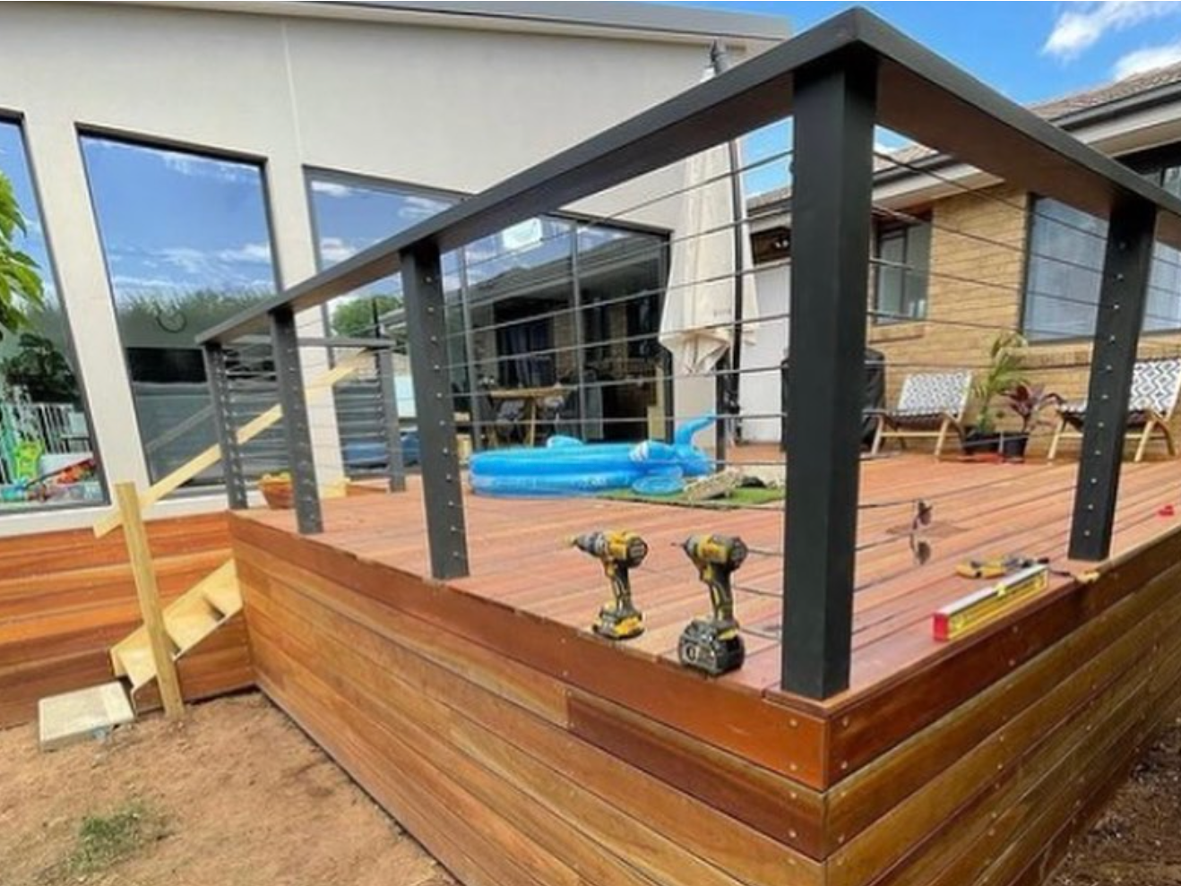 A wooden deck with a metal railing is being built in front of a house.