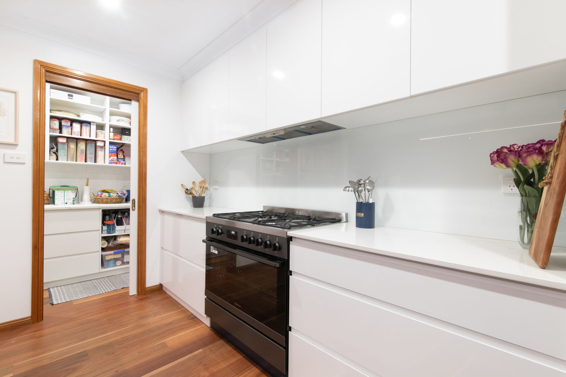 A kitchen with white cabinets , a stove , and a pantry.