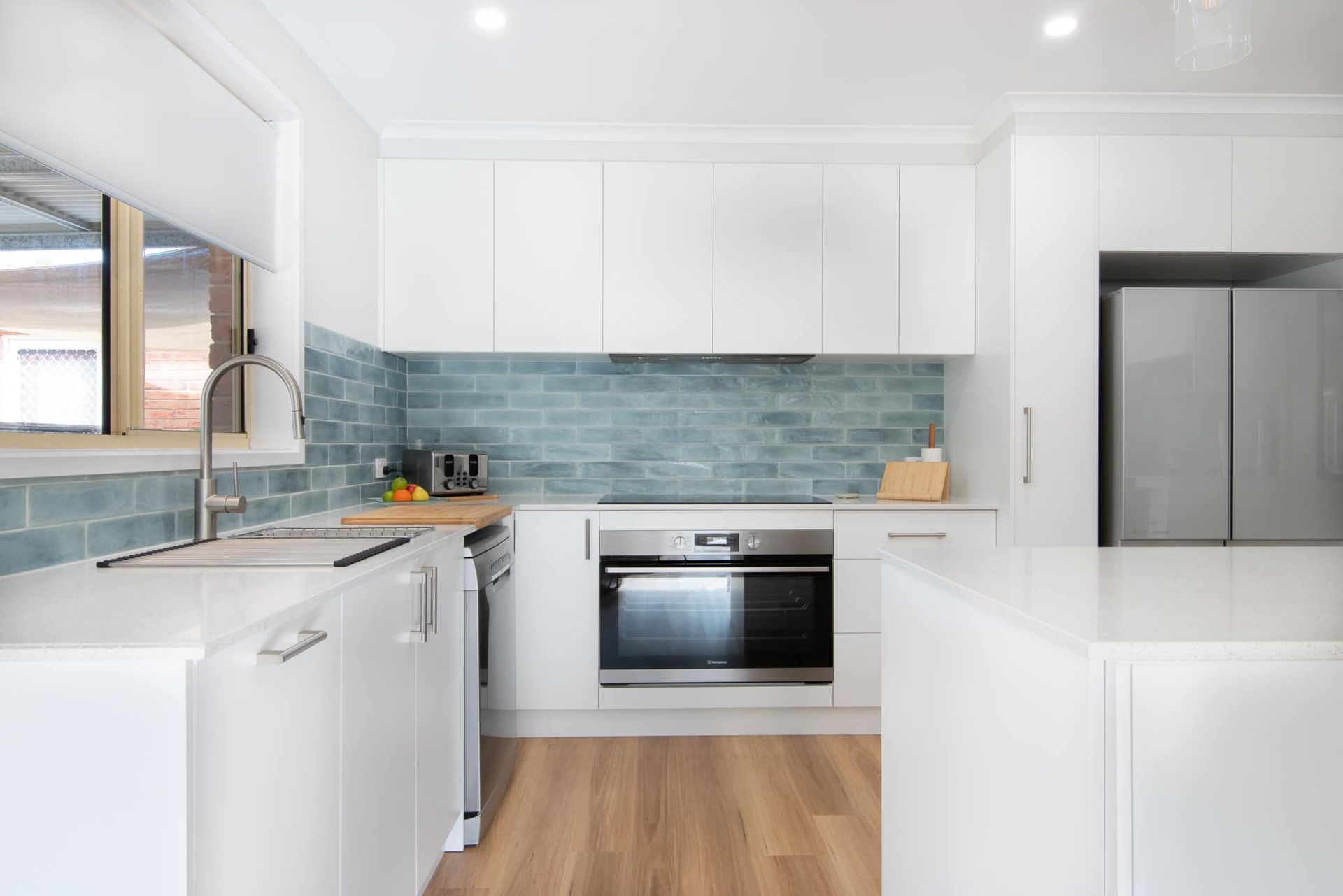A kitchen with white cabinets , stainless steel appliances , a sink , and a refrigerator.