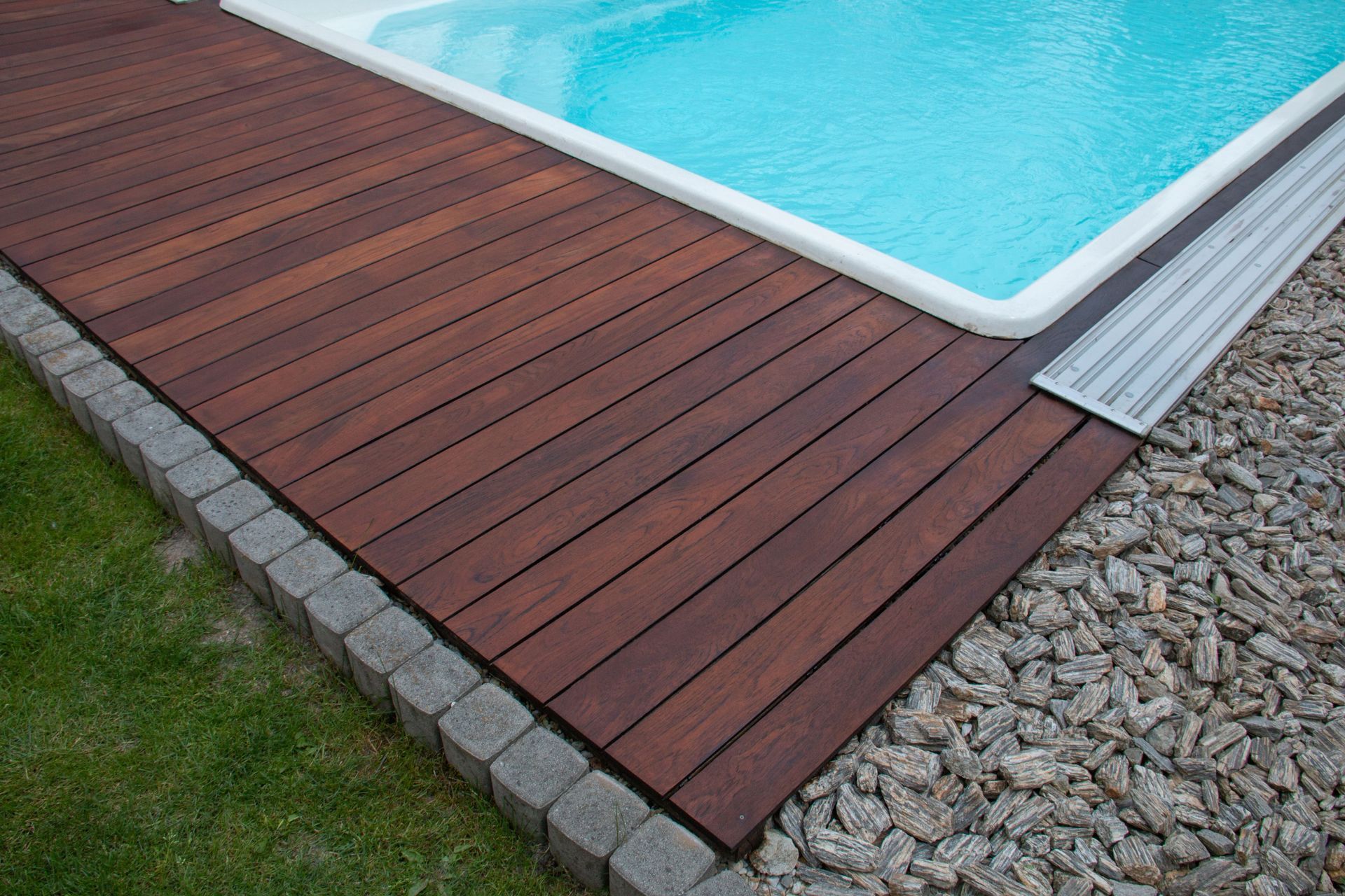 A wooden deck is next to a swimming pool.