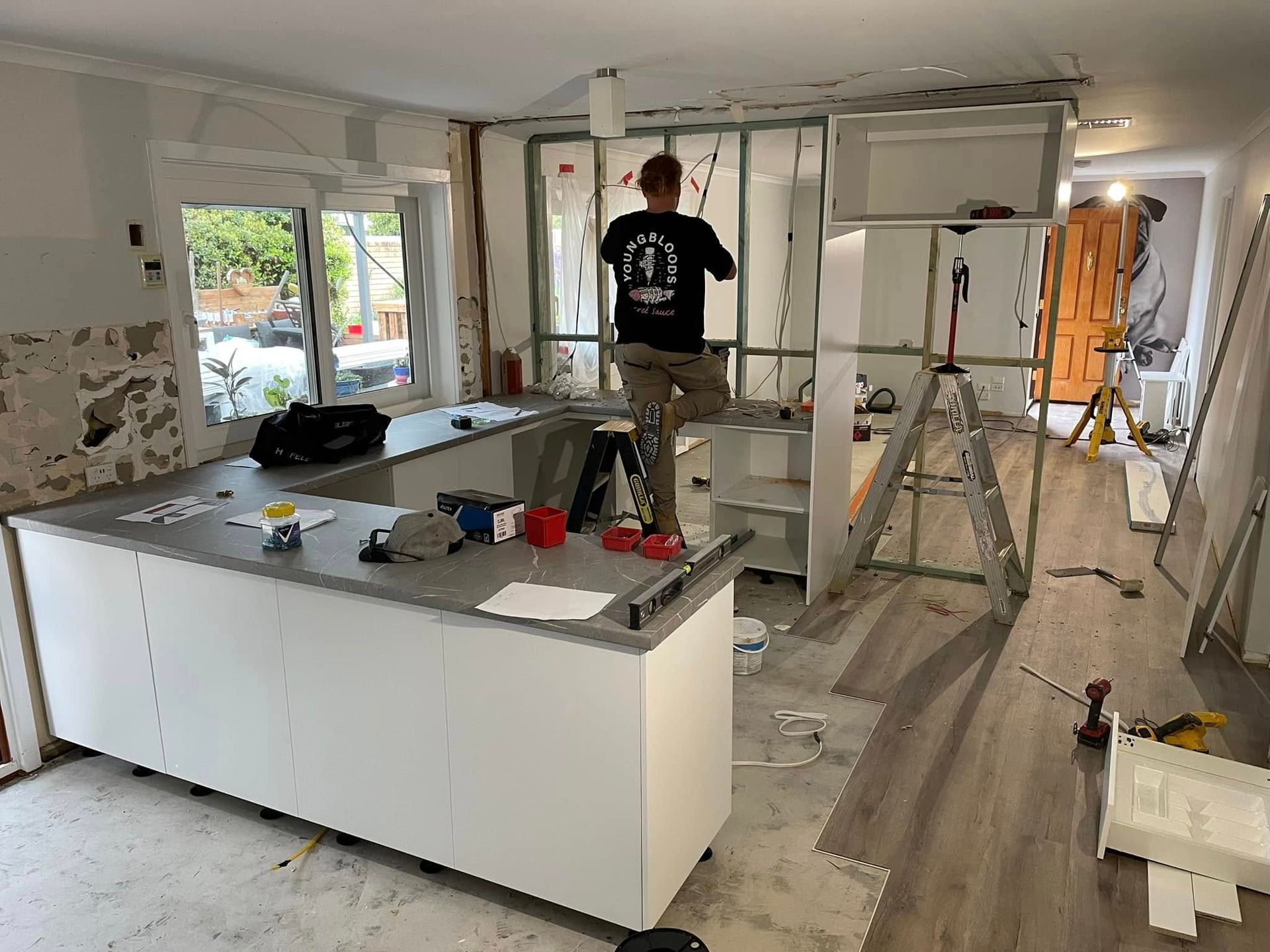 A man is standing on a ladder in a kitchen under construction.