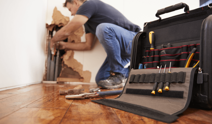 A man is working on a wall next to a tool bag filled with tools.