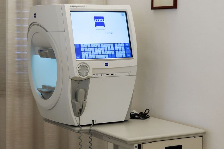 Un apparecchio per l'esame della vista con uno schermo di computer, una sedia nera e un tavolo in una stanza bianca.