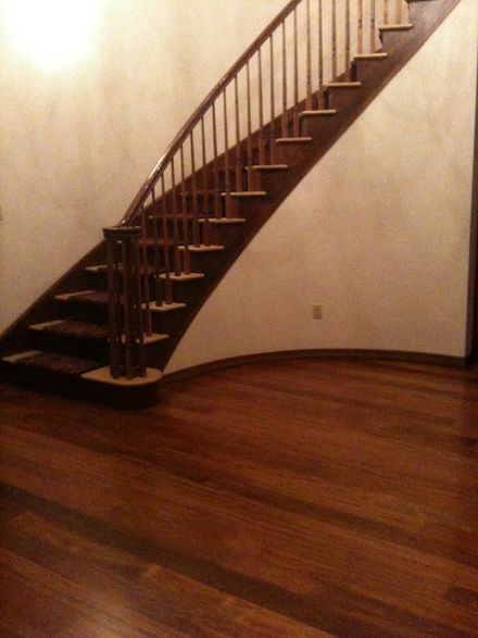 A curved wooden staircase with railings stands against a light-colored wall above dark wood flooring.