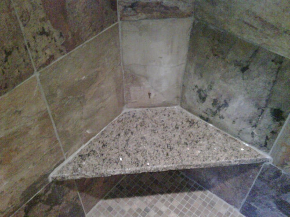 A granite triangular shower corner shelf installed against beige and grey tiled walls in a bathroom.