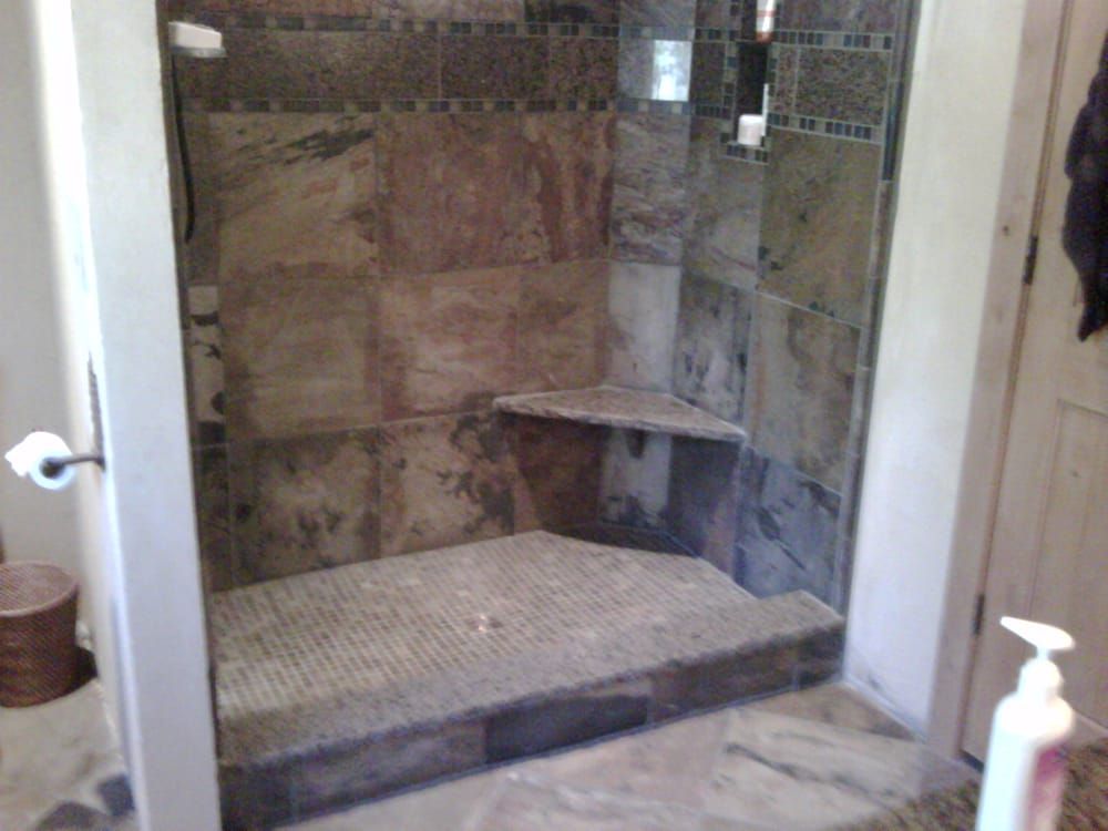 A walk-in shower with earthy, multi-toned stone tile walls, a mosaic floor, a corner bench, and a low step entry.