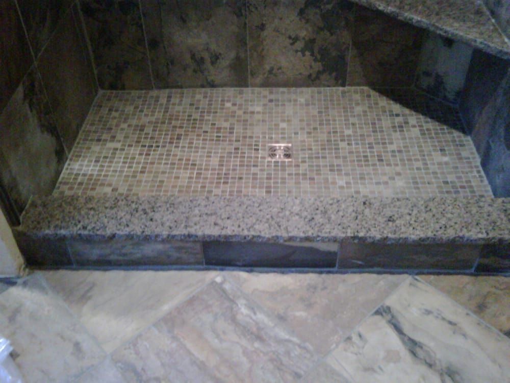 A tiled walk-in shower with a mosaic floor, a central drain, and a granite threshold step.